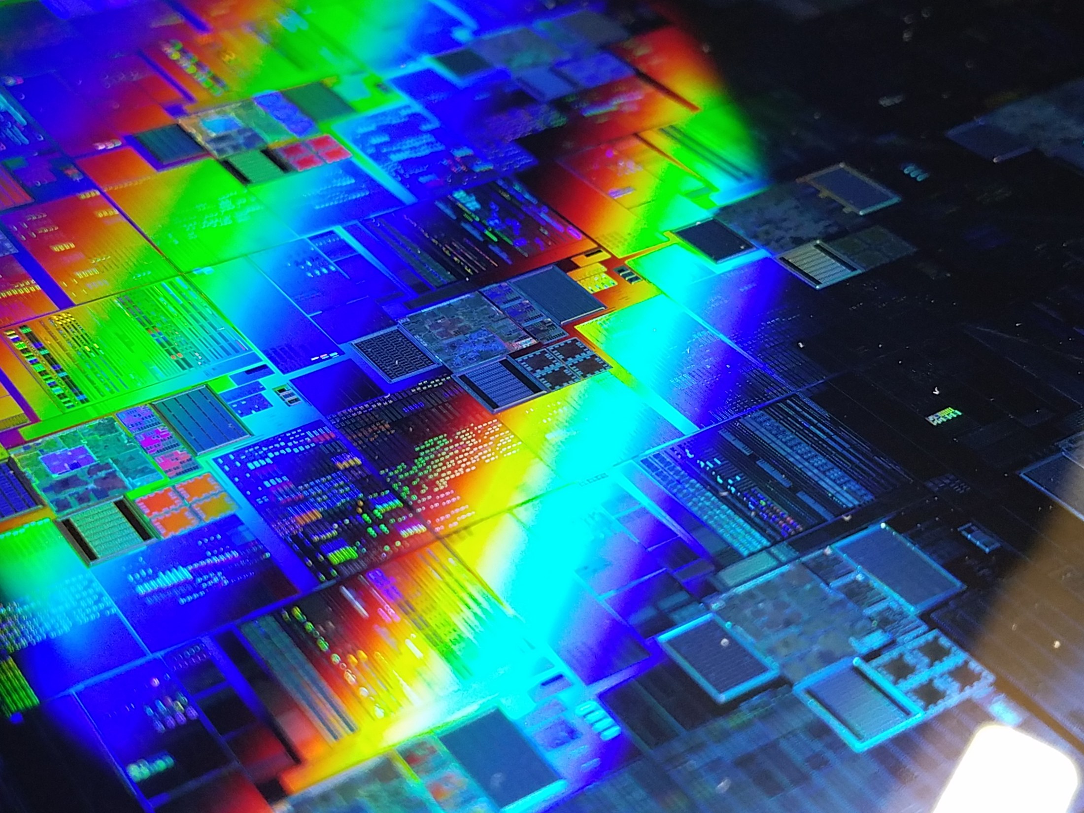 Foto van een siliciumwafer met regelmatige chipstructuren en kleurrijke lichtreflecties
